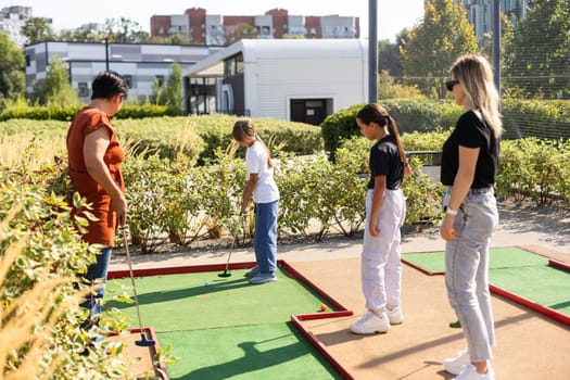 Mother and her little daughter practicing to hit the ball at the course. High quality photo