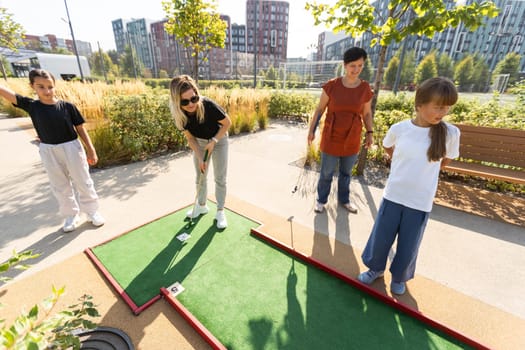 Cute school girl playing mini golf with family. Happy toddler child having fun with outdoor activity. Summer sport for children and adults, outdoors. Family vacations or resort. High quality photo