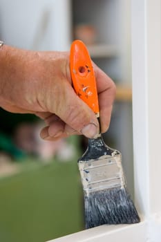 Close-up hand with brush in hand and painting a white frame