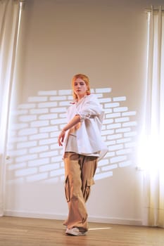 A dancer performs dynamic movements in a spacious studio. Bright sunlight streams through sheer curtains, casting interesting shadows on the floor and walls.