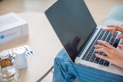 Business female sick she taking pills for flu while work with laptop keyboard, Asian sick woman covered blanket suffering from covid-19 virus but still working at home with laptop computer