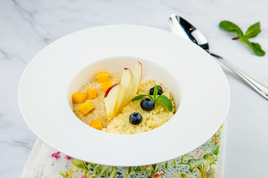 porridge with pieces of apple, mango, berries and mint