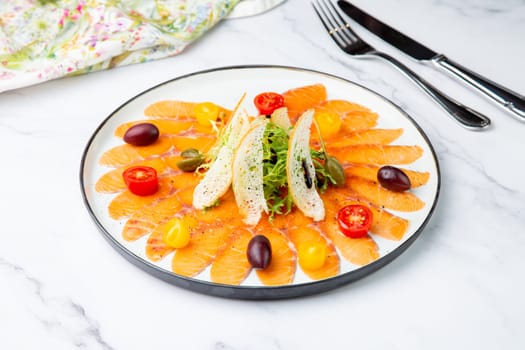 thinly sliced ​​pieces of smoked salmon with cherry tomatoes, olives and herbs on a white plate. view from above. High quality photo