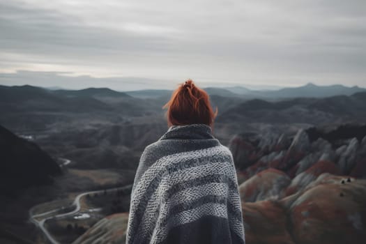 Woman with red hair in grey knitted sweater looking to high mountains landscape, view from back. Neural network generated in May 2023. Not based on any actual person, scene or pattern.