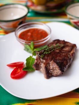 beef steak with tomato sauce, tomatoes and herbs in oriental style on a table with a teapot and a cup for tea. High quality photo