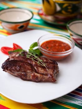beef steak with tomato sauce, tomatoes and herbs in oriental style on a table with a teapot and a cup for tea. High quality photo