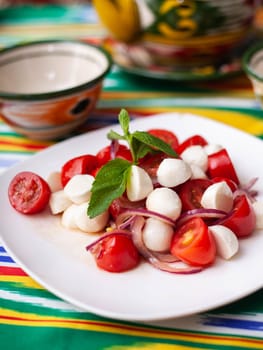 caprese salad with mazzarella tomatoes and herbs in oriental style on a table with a teapot and a cup for tea. High quality photo