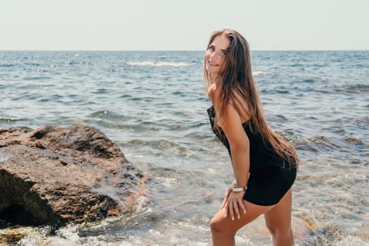 Woman travel sea. Young Happy woman in a long red dress posing on a beach near the sea on background of volcanic rocks, like in Iceland, sharing travel adventure journey