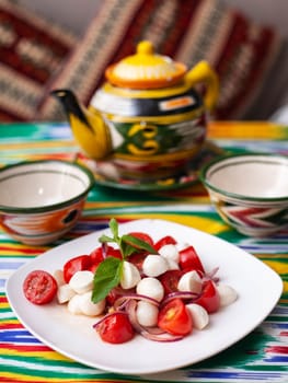 caprese salad with mazzarella tomatoes and herbs in oriental style on a table with a teapot and a cup for tea. High quality photo