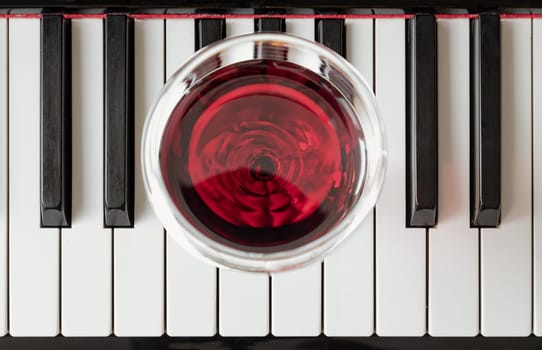 Glass of red wine on piano keyboard. Music and wine concept, Top view, Space for text, Selective focus.