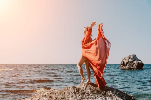 Woman travel sea. Young Happy woman in a long red dress posing on a beach near the sea on background of volcanic rocks, like in Iceland, sharing travel adventure journey