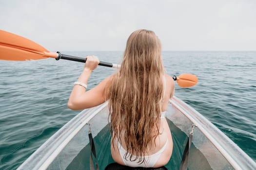 Woman in kayak back view. Happy young woman with long hair floating in transparent kayak on the crystal clear sea. Summer holiday vacation and cheerful female people having fun on the boat.