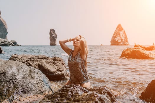 Woman travel sea. Young Happy woman in a long red dress posing on a beach near the sea on background of volcanic rocks, like in Iceland, sharing travel adventure journey