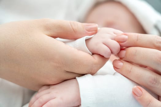 Close-up captures the fragile moment of an unwell newborn baby holding onto mother's finger, with a wet towel on the brow