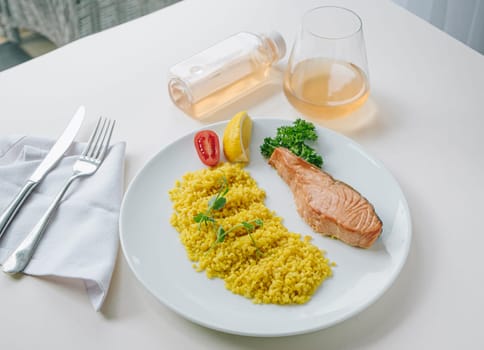 proper nutrition, daily diet, weight loss. greens, tomatoes, salmon steak with lemon and couscous garnish on a plate.