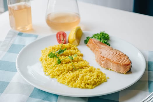 proper nutrition, daily diet, weight loss. greens, tomatoes, salmon steak with lemon and couscous garnish on a plate.