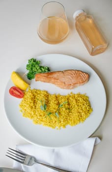 proper nutrition, daily diet, weight loss. greens, tomatoes, salmon steak with lemon and couscous garnish on a plate.
