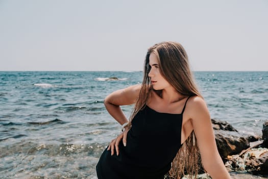 Woman travel sea. Young Happy woman in a long red dress posing on a beach near the sea on background of volcanic rocks, like in Iceland, sharing travel adventure journey