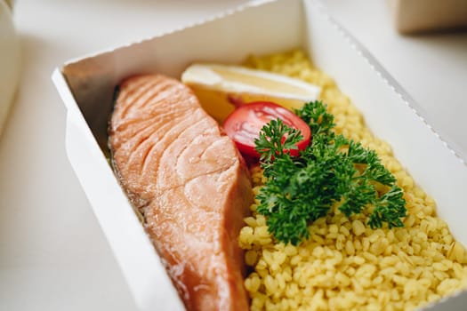 food in containers. proper nutrition, daily diet, weight loss. greens, tomato, lemon salmon steak with couscous side dish.