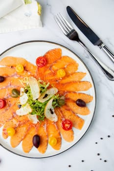 thinly sliced ​​pieces of smoked salmon with cherry tomatoes, olives and herbs on a white plate. view from above. High quality photo