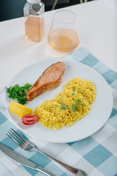 proper nutrition, daily diet, weight loss. greens, tomatoes, salmon steak with lemon and couscous garnish on a plate.