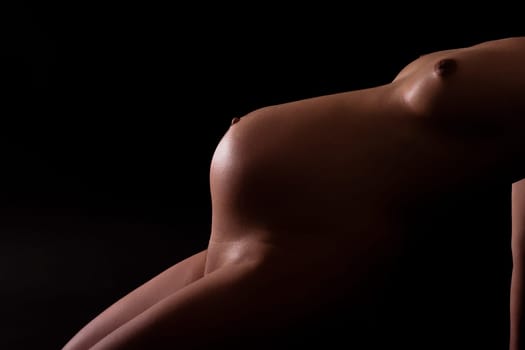 Pregnant attractive woman (8th month) leaning on (looks like a staircase). Shoulders to legs visible. Artistically illuminated. Black background.