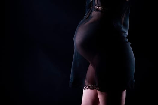 Pregnant attractive woman (8th month) in see-through dress. Black background.