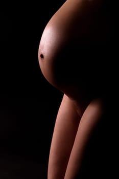 Baby bump and thighs. Pregnant attractive woman (8th month). Artistically illuminated. Black background.