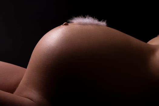 Pink feather on baby belly. Pregnant attractive woman (8th month). Black background.