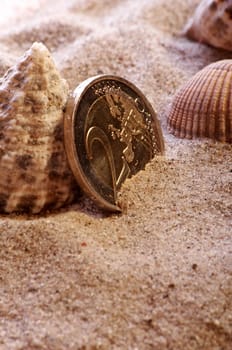 golden shiny 2 Euro piece with sand and shells as symbolism for holiday pay / holiday fund