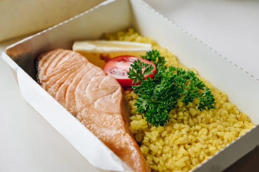 food in containers. proper nutrition, daily diet, weight loss. greens, tomato, lemon salmon steak with couscous side dish.