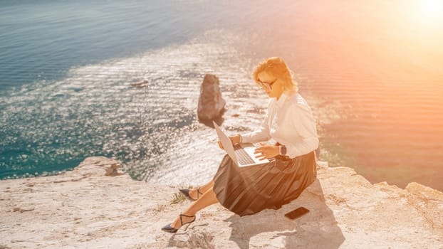 Business woman on nature in white shirt and black skirt. She works with an iPad in the open air with a beautiful view of the sea. The concept of remote work