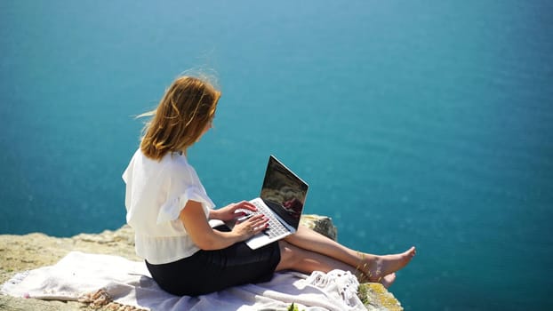 Freelance woman sea. working on a laptop by the sea, typing away on the keyboard while enjoying the beautiful view, highlighting the idea of remote work