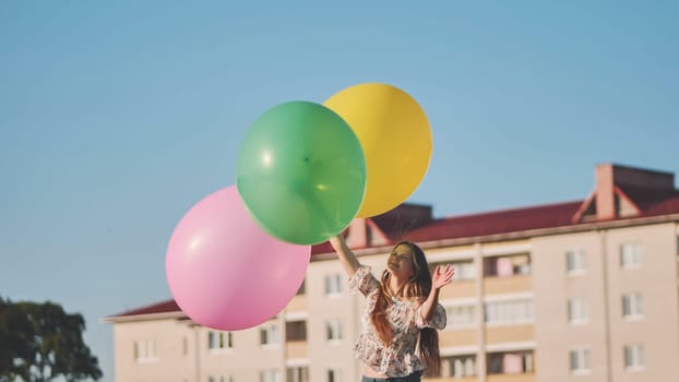 Happy girl with big with colorful balloons posing on the background of city houses