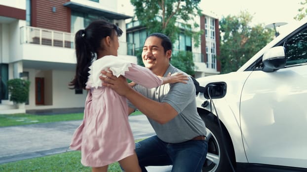 Progressive father and daughter installing plug from home charging station for electric vehicle. Future eco-friendly car with EV cars powered by renewable source of clean energy.