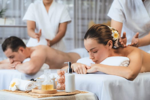 Caucasian couple customer enjoying relaxing anti-stress spa massage and pampering with beauty skin recreation leisure in day light ambient salon spa at luxury resort or hotel. Quiescent