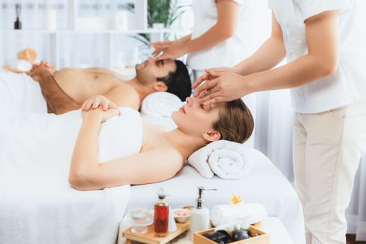 Caucasian couple enjoying relaxing anti-stress head massage and pampering facial beauty skin recreation leisure in dayspa modern light ambient at luxury resort or hotel spa salon. Quiescent