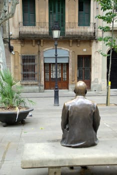 Figure on bench in front of house in a square in Barcelona