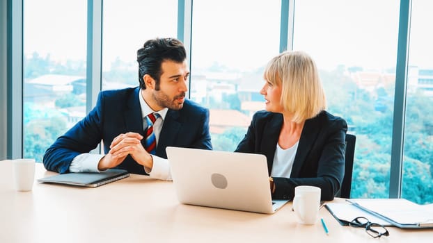 Two business people talk project strategy at office meeting room. Businessman discuss project planning with colleague at modern workplace while having conversation and advice on financial report. Jivy