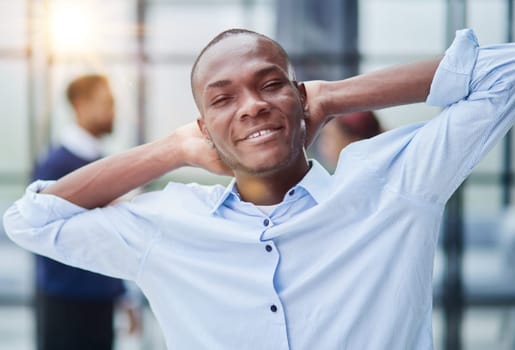 Happy african american young businessman holding hands behind head looking at camera