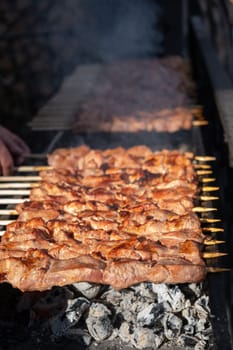 A lot of juicy meat kebabs in a row on the grill. Meat pieces strung on wooden skewers on the grill. The process of cooking kebabs with a lot of smoke. Cooking in nature