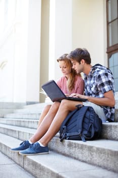 University, education and students with laptop on building steps for team project research. Learning, studying and gen z friends online on stairs with book for assignment, exam or homework discussion.