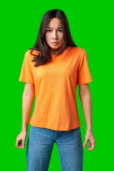 A woman stands confidently with her hands clenched, wearing a bright orange shirt and blue jeans. Her expression reflects determination and strength against a vivid green backdrop.