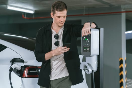 Young man travel with EV electric car to shopping center parking lot charging in downtown city showing urban sustainability lifestyle by green clean rechargeable energy of electric vehicle innards