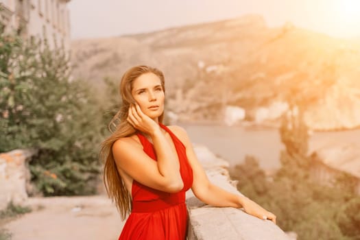 Woman red dress. Summer lifestyle of a happy woman posing near a fence with balusters over the sea