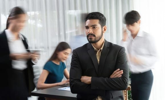 Businessman portrait poses confidently with diverse coworkers in busy meeting room in motion blurred background. Multicultural team works together for business success. Concord