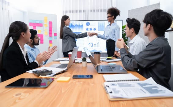 Diverse coworker celebrate with handshake and teamwork in corporate workplace. Happy business people united by handshaking after successful meeting or business presentation on data analysis. Concord