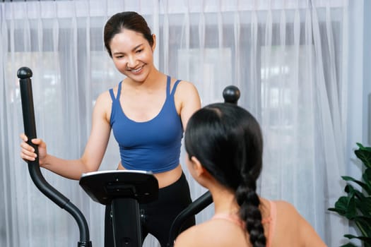 Energetic and strong athletic asian woman running on elliptical running machine at home with workout buddy or trainer. Pursuit of fit physique and commitment to healthy lifestyle. Vigorous