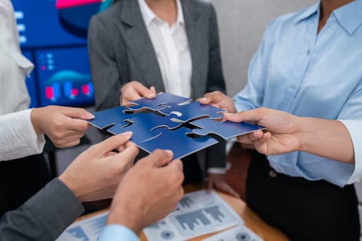 Corporate officer worker collaborate in office, connecting puzzle pieces with report paper on table as partnership and teamwork. Unity and synergy in business concept by merging jigsaw puzzle. Concord