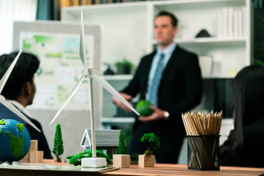 Mockup electric car with eco-friendly energy infrastructure on table with blurred background of productive business team meeting to contribute natural preservation and sustainable future. Quaint